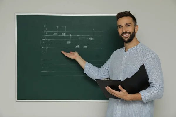 教室に音楽ノートを持つ緑の黒板の近くの教師 — ストック写真