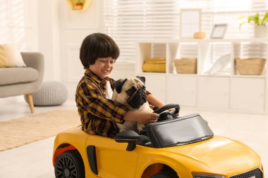 Evdeki oyuncak arabasında köpeği olan küçük çocuk.