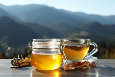 Taze aromatik bal ve bir fincan sıcak çay, dağ manzarasına karşı gri ahşap masada.