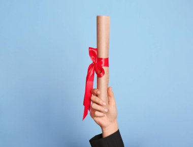 Açık mavi arka planda kırmızı kurdeleli öğrenci diploması, yakın plan.