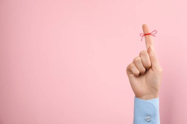 Pembe arkaplanda hatırlatma olarak bağlı kırmızı yay ile işaret parmağı gösteren kadın, yakın plan, metin için boşluk