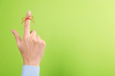 Açık yeşil arka planda bağlı kırmızı kurdeleli işaret parmağı olan bir kadın, yakın plan. Metin için boşluk