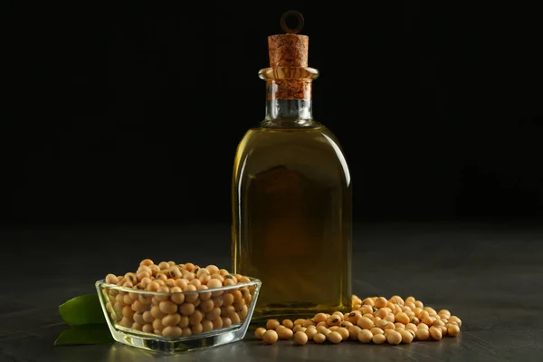 Glass bottle of oil, leaves and soybeans on grey table