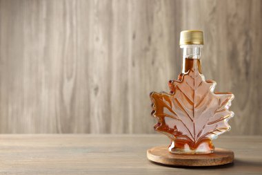 Leaf shaped bottle of tasty maple syrup on wooden table, space for text clipart
