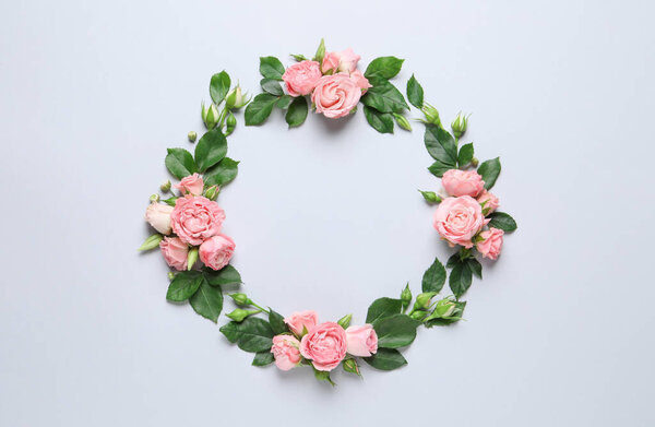 Wreath made of beautiful flowers and green leaves on light background, flat lay. Space for text