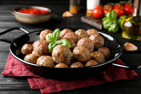 Tasty cooked meatballs with basil on black wooden table