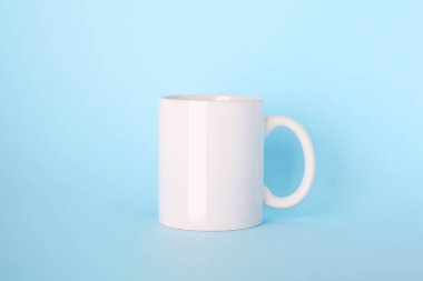 Açık mavi arkaplanda boş beyaz seramik bardak