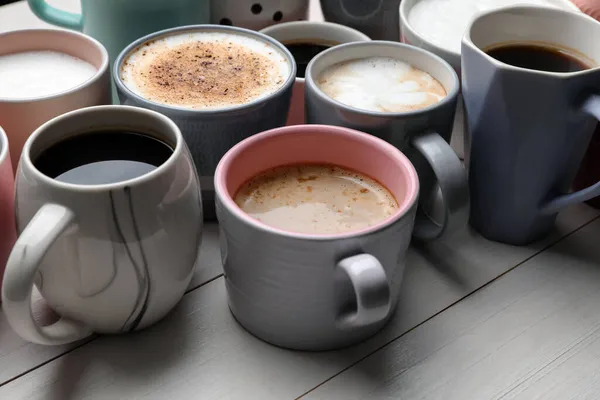 许多不同的杯子 白木桌上有香浓的热咖啡 — 图库照片