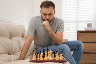 Evdeki kanepede tek başına satranç oynayan düşünceli genç adam.