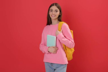 Sırt çantası ve kırmızı arka plan kitabı olan genç bir öğrenci.