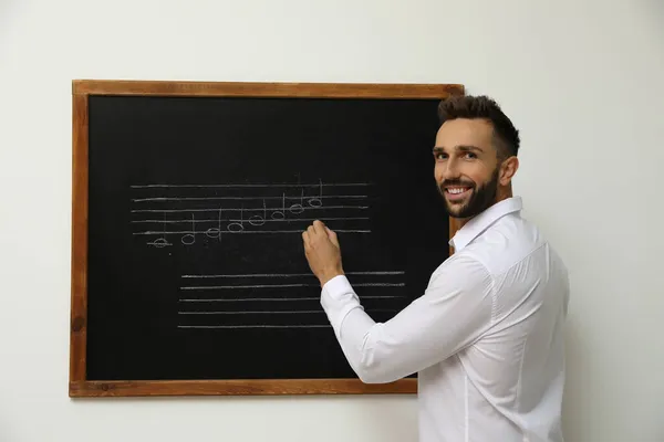 先生は教室で黒板にチョークで楽譜を書く — ストック写真