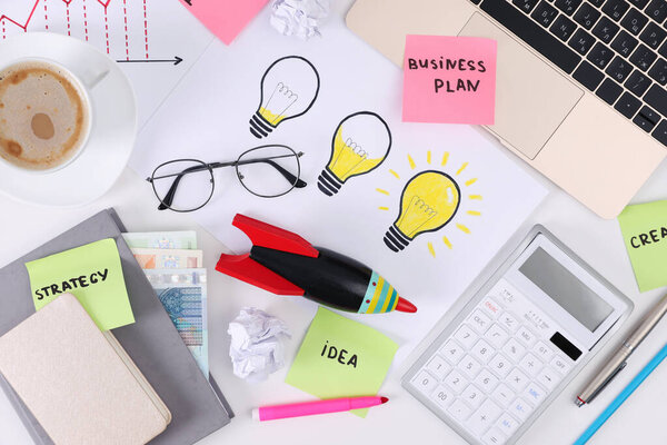 Квартира лежала композиция с канцелярскими принадлежностями, деньгами и игрушечной ракетой на белом столе. Концепция запуска