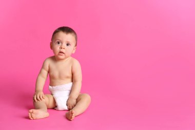 Pembe arka planda oturan kuru, yumuşak bezli şirin bir bebek. Metin için boşluk
