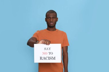 Afro-Amerikalı bir adam açık mavi arka planda ırkçılığa hayır deyin tabelasını tutuyor.