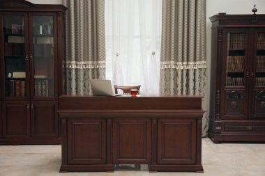 Kütüphane okuma odası masasında ahşap kitaplıklar ve dizüstü bilgisayar var.