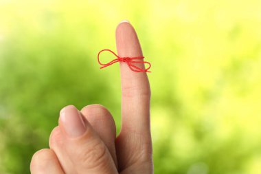 Bulanık yeşil arkaplanda hatırlatıcı olarak bağlı kırmızı yay ile işaret parmağı gösteren kadın, yakın plan