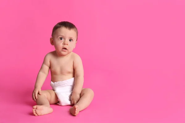 可爱的婴儿穿着干爽柔软的尿布坐在粉红的背景上 案文的篇幅 — 图库照片