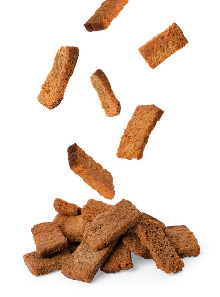 Delicious crispy rusks falling into pile on white background