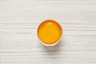Kırık tavuk sarısı, yumurta kabuğu, beyaz ahşap masa, üst manzara.