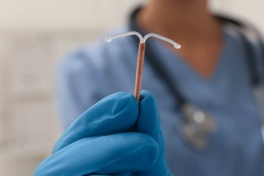 Doktor uterus içi doğum kontrol cihazını arka planda tutuyor. Yakın plan.