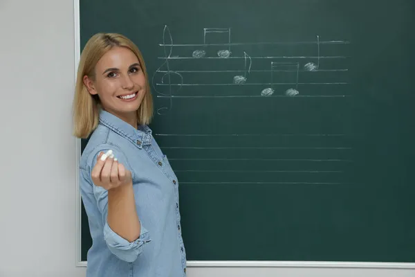 教室に音楽ノートを持つ緑の黒板の近くの教師 — ストック写真