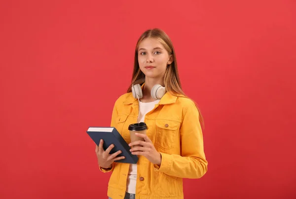 本を持つ10代の学生 赤の背景にコーヒーとヘッドフォンのカップ — ストック写真