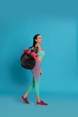 Spor çantalı güzel bir kadın ve açık mavi arka planda yoga minderi.
