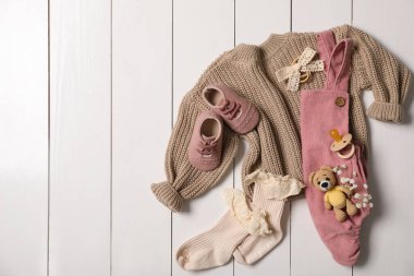 Çocuk kıyafetleri, ayakkabıları ve oyuncaklarıyla beyaz ahşap masa üzerinde düz bir kompozisyon vardı. Metin için boşluk