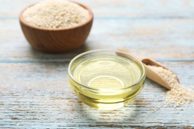 Açık mavi ahşap masada taze susam yağı ve tohumlar, yakın plan.