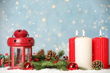 Yanan mumların üzerine yağan kar ve açık mavi arkaplan ve bulanık ışıklar karşısında şenlikli bir dekor. Noel arifesi