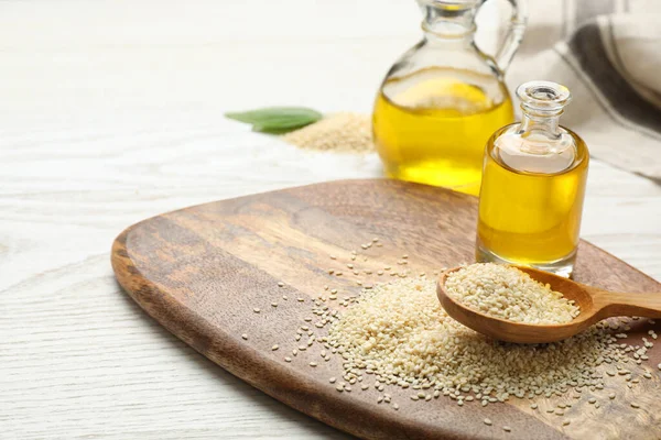 Fresh sesame oil and seeds on white wooden table. Space for text