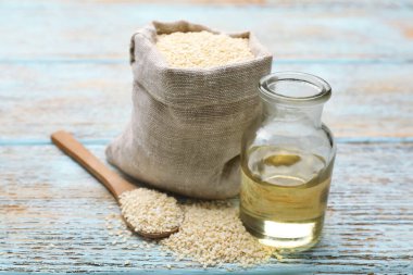 Açık mavi ahşap masada taze susam yağı ve tohumlar, yakın plan.