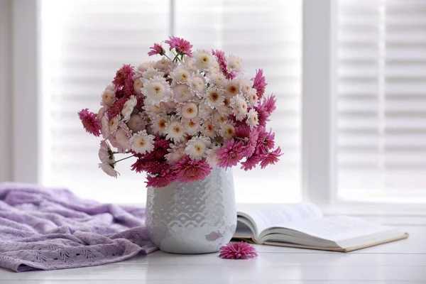 Güzel bir buket ve pencerenin yanındaki beyaz ahşap masada açık bir kitap.