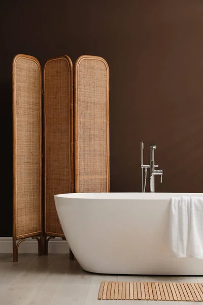 房间里靠近棕色墙壁的现代陶瓷浴缸和折叠式屏风 — 图库照片