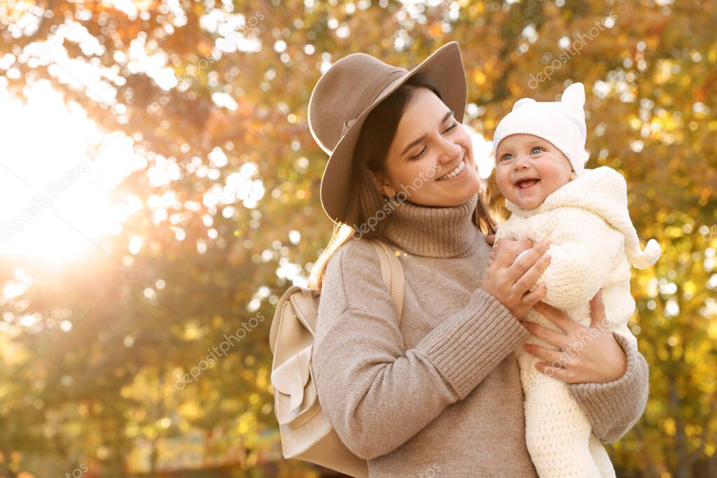 Happy mother with her baby daughter outdoors on autumn day, space for text