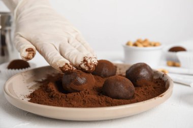 Çikolata yer mantarlarını beyaz masada kakao tozuyla kaplayan şekerci, yakın plan.