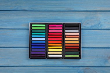 Açık mavi ahşap masadaki kutuda renkli pasteller, üst manzara. Çizim malzemeleri