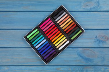 Açık mavi ahşap masadaki kutuda renkli pasteller, üst manzara. Çizim malzemeleri