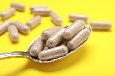 Sarı arka planda kaşık içinde jelatin kapsüller, yakın plan.