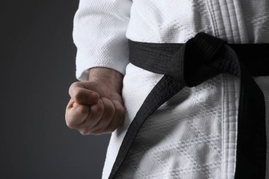 Gri arka planda kimono ve siyah kuşak giyen karate koçu, yakın plan.