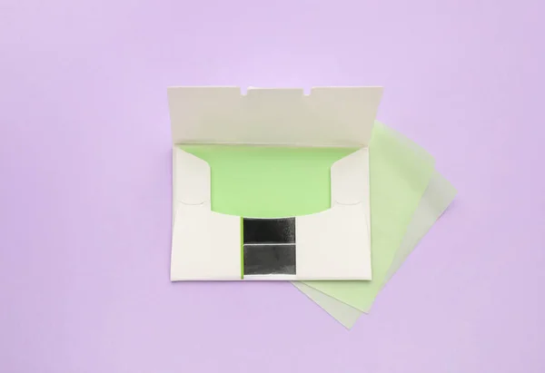 Package with facial oil blotting tissues on violet background, flat lay. Mattifying wipes