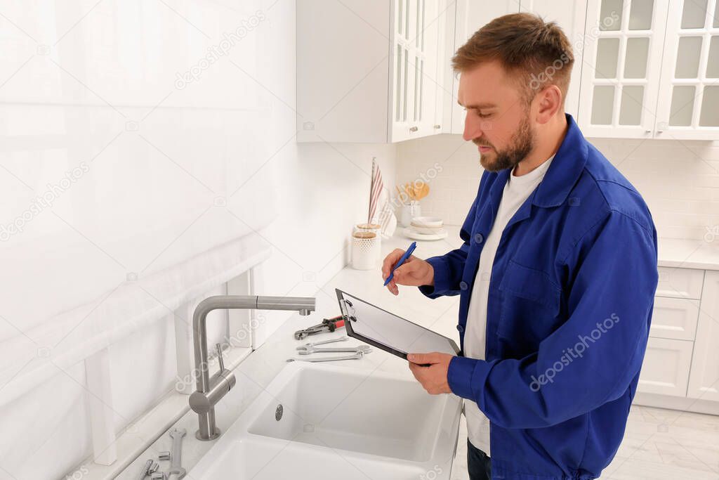 Plumber with clipboard checking water tap in kitchen