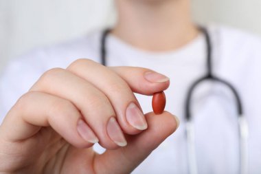 Doctor holding red pill, closeup. Anemia concept clipart