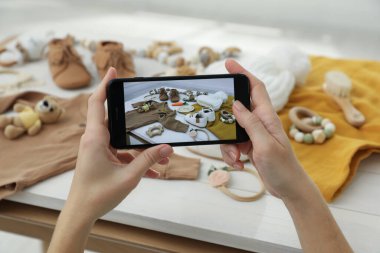 Beyaz ahşap masada bebek kıyafetlerinin fotoğrafını çeken kadın, yakın plan.