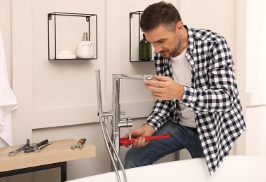 Adam banyoya duş başlığıyla musluk kuruyor.