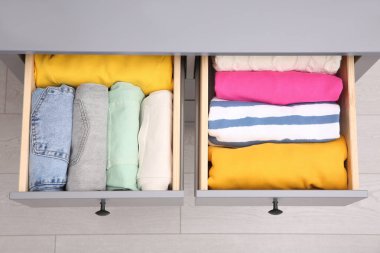 Open drawers with folded clothes indoors, top view. Vertical storage clipart