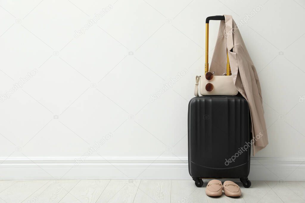 Packed suitcase, shoes, jacket and accessories near white wall indoors. Space for text