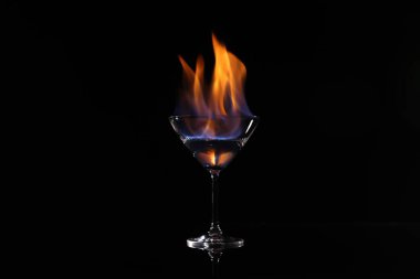 Siyah arka planda yanan votkalı kokteyl bardağı.