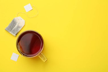 Sarı arka planda çay poşetleri ve cam bardak sıcak içecek. Metin için boşluk
