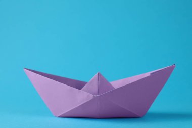 Açık mavi arka planda el yapımı menekşe kağıt tekne. Origami sanatı